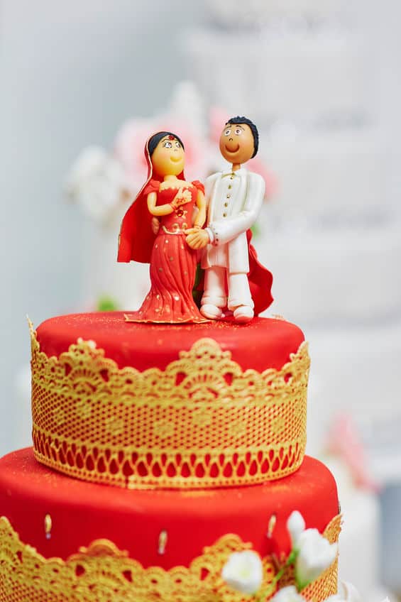 Beautiful red and yellow wedding cake in Indian style with bride and groom figurines on top