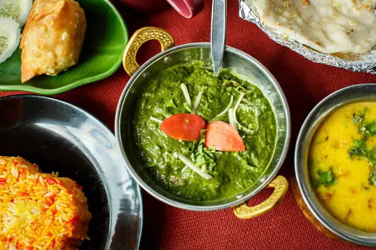 Indian food on a table including saag, naan bread, rice and samba