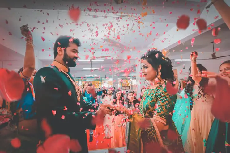 hindu bride and groom holding hands with indian wedding guests showering them with flower petals